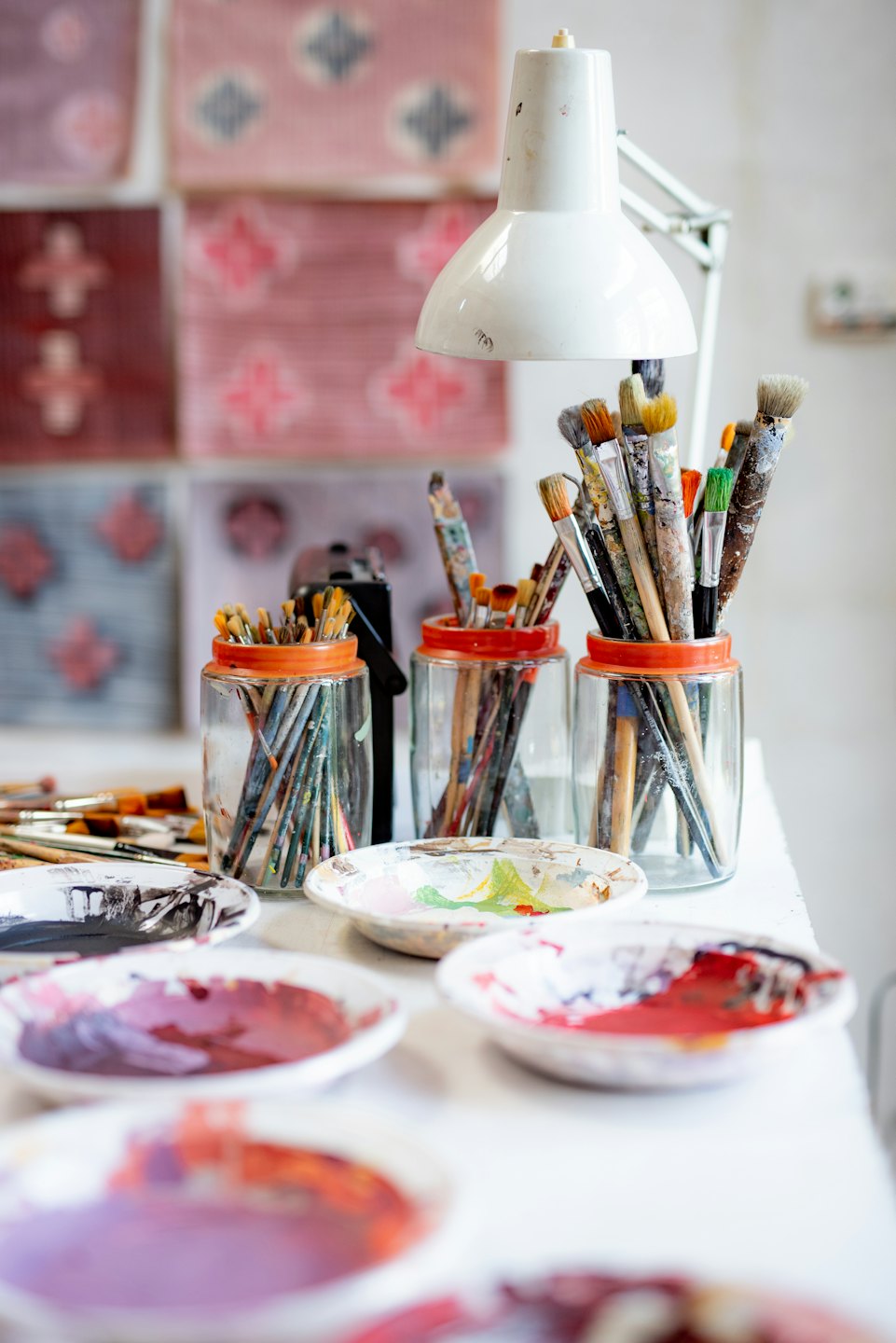 Artist's workbench with paint brushes in jars and palettes of mixed paint.
