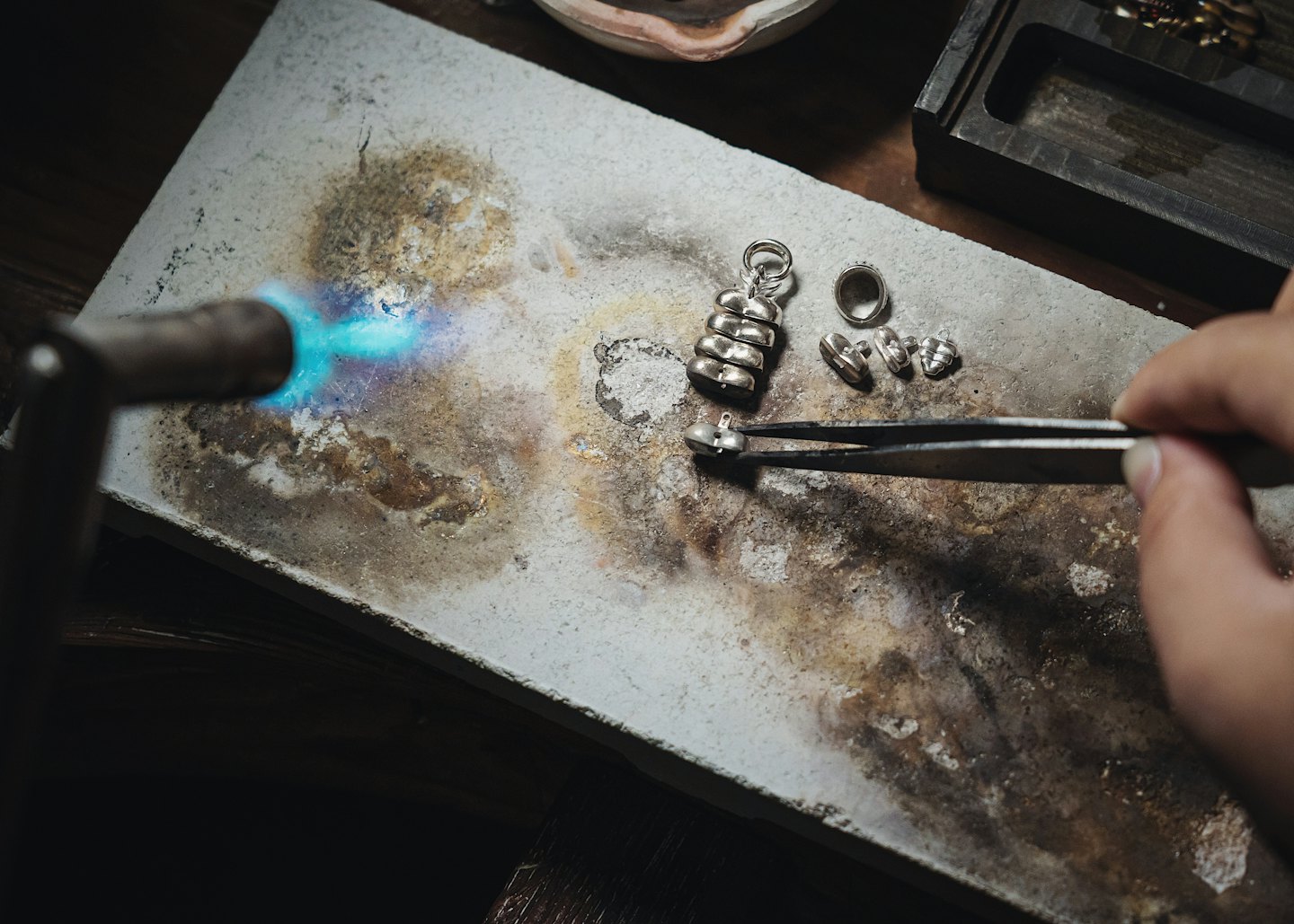 An artisan uses a torch to solder small silver jewelry components.